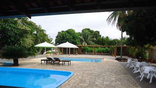 An outdoor pool area with stone flooring, lounge chairs, umbrellas, and white plastic chairs. - Pantanal Hotel (Miranda)