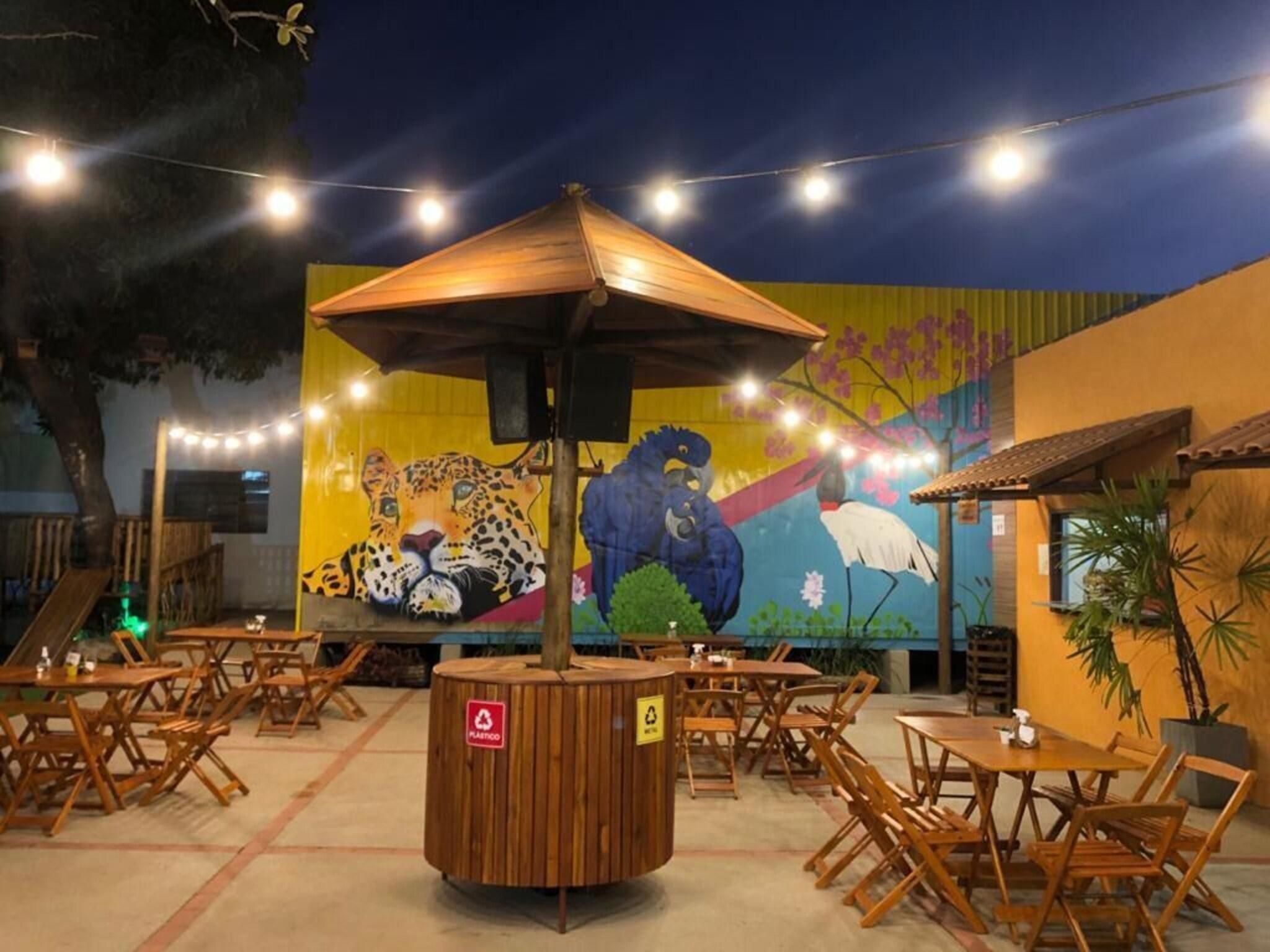 An outdoor seating area with tables and chairs, a central wooden structure, and a mural with wildlife on the wall.