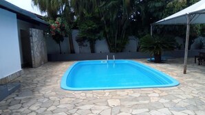 A rectangular swimming pool with a stone tile deck, surrounded by a white wall and palm trees. - Pantanal Hotel (Miranda)