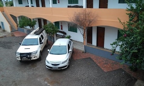 A building with two cars parked in front, a staircase, and a tree.