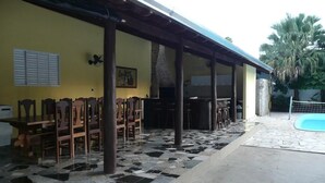 A covered outdoor area with a tiled floor, wooden chairs, a pool, and a yellow wall with a picture. - Pantanal Hotel (Miranda)