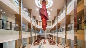 A modern atrium with a central red sculpture, multiple levels with glass railings, and rows of seating. - Cemerlang (Bandung)