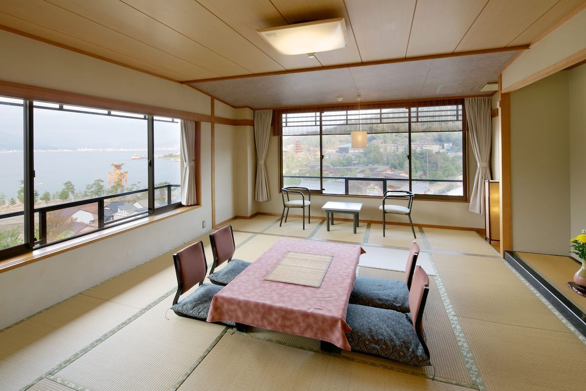 A traditional Japanese room with tatami flooring, a low table with a pink tablecloth, and a view of a body of water and buildings.