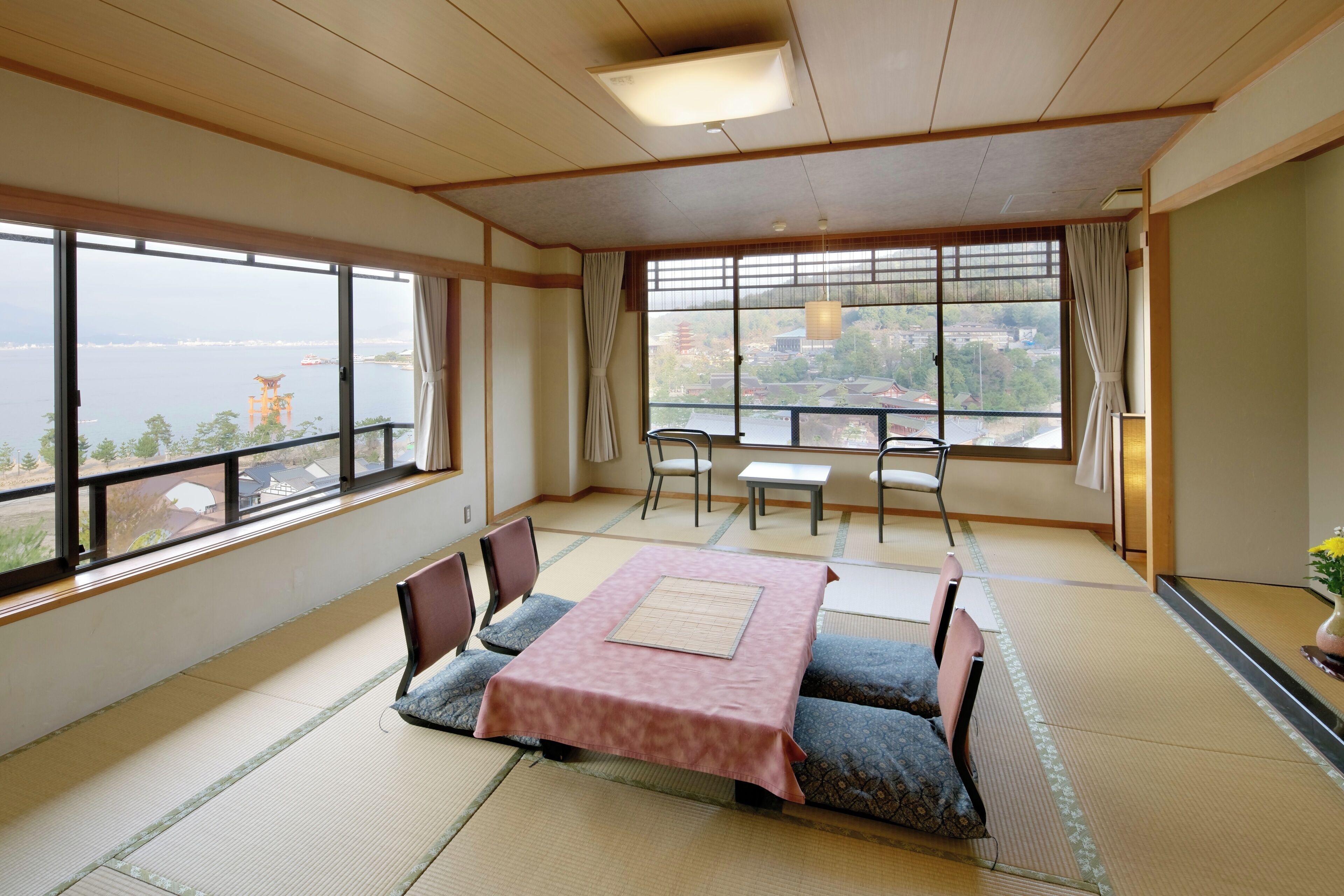 Una habitación japonesa tradicional con suelo de tatami, una mesa baja con mantel rosa y vista a un cuerpo de agua.