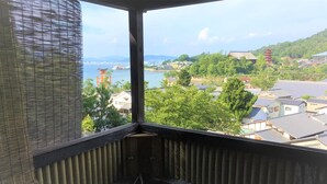 A room with a view of a body of water, buildings, and greenery. - Jukeiso (Hatsukaichi)