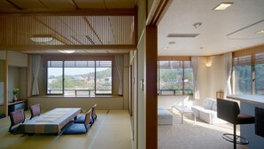 A traditional Japanese-style room with tatami flooring, a low table with cushions, and a view of a mountainous landscape through large windows. - Jukeiso (Hatsukaichi)