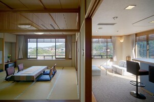 Una habitación tradicional japonesa con suelo de tatami, una mesa baja con cojines y vistas a un paisaje montañoso a través de amplios ventanales.