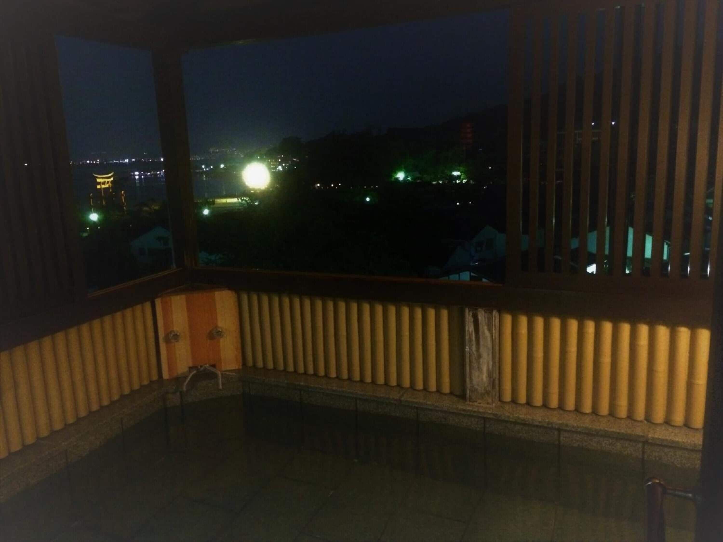 A room with a view of a cityscape at night, featuring a large window with blinds and a radiator.