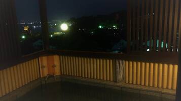 A room with a view of a cityscape at night, featuring a large window with blinds and a radiator.