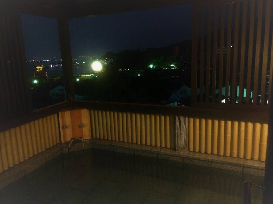 A room with a view of a cityscape at night, featuring a large window with blinds and a radiator.