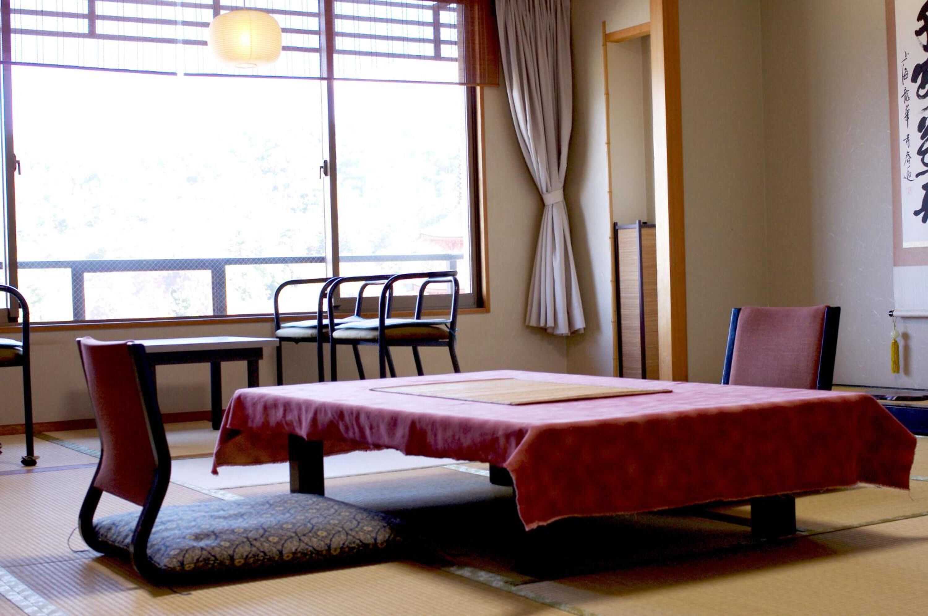 Ein traditioneller japanischer Raum mit Tatami-Böden, einem niedrigen Tisch mit roter Tischdecke und einem Fenster mit Shoji-Schirm.