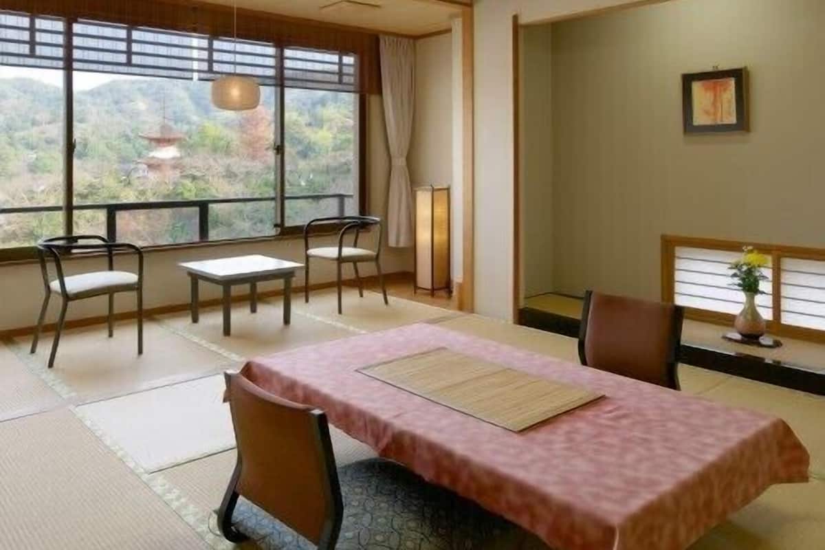 A traditional Japanese-style room with tatami flooring, a low table with a pink tablecloth, and a view of a mountainous landscape through large windows.