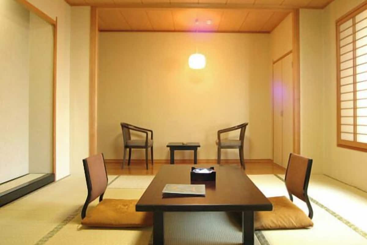 A traditional Japanese room with tatami flooring, a low table, and two chairs.