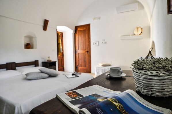 A bedroom with a bed, a wooden door, a white wall, a small shelf, and a wicker basket with a cup and saucer.