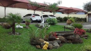 A garden area with a car parked under a canopy, surrounded by rocks, plants, and a small rabbit statue. - Abib Hotel (IRATI)