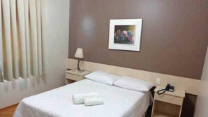 A neatly made bed with white linens and two rolled towels, a bedside table with a lamp, a framed picture on the wall, and a telephone on the nightstand. - Abib Hotel (IRATI)