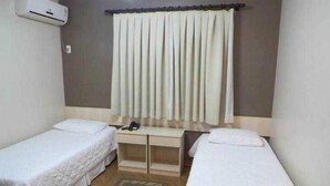 A small, clean room with two single beds, a desk with a telephone, and a window with curtains. - Abib Hotel (IRATI)