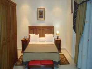 Un dormitorio con cama, dos mesitas de noche, un armario de madera, un cuadro enmarcado en la pared y una cortina.