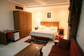 Una habitación de hotel con cama, escritorio, armario, sofá rojo y una mesita.