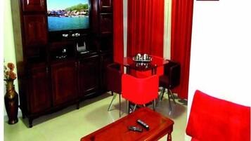 A living room with a flat-screen TV, red chairs, a wooden coffee table, and a red curtain.