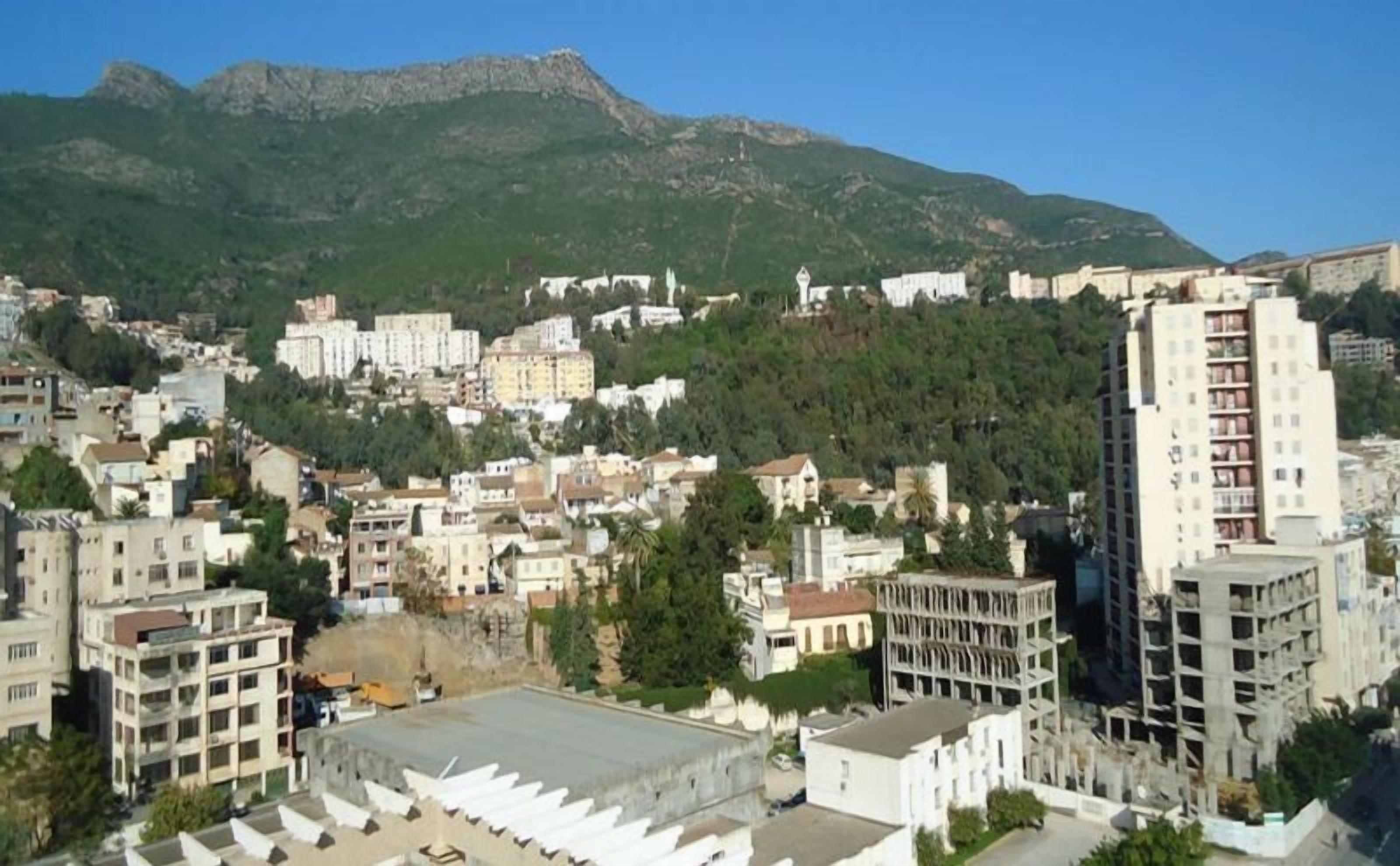 A cityscape with buildings, a large open area, and mountains in the background.