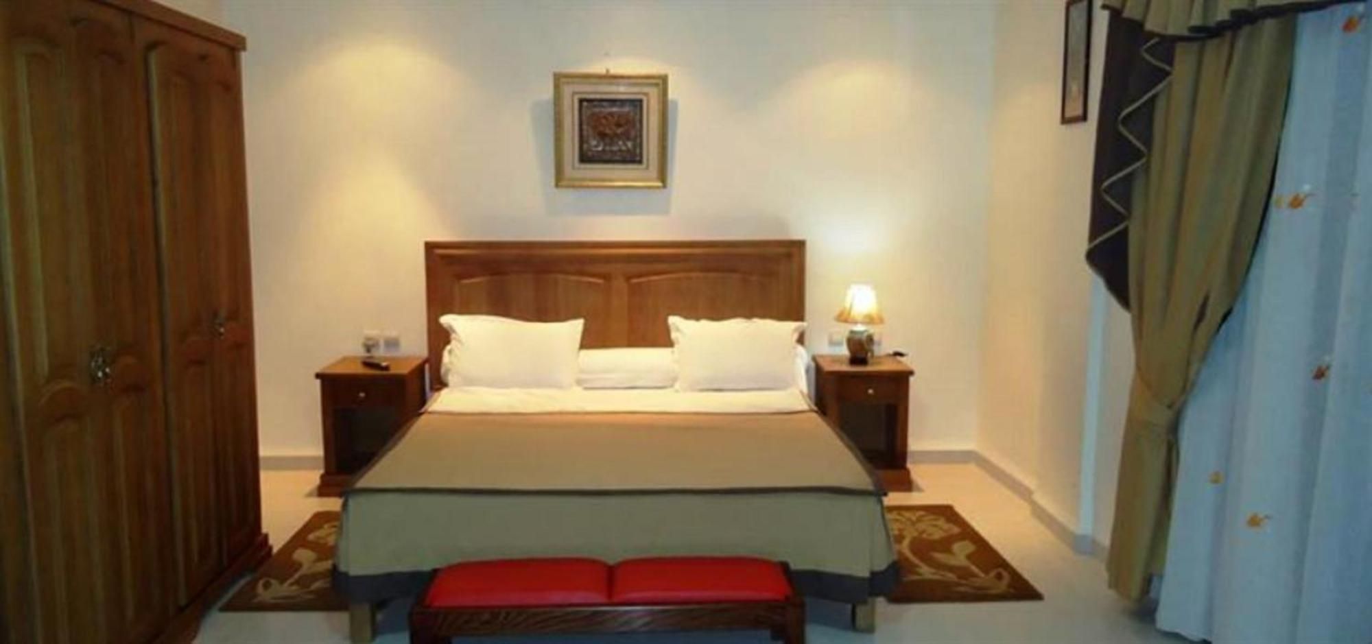 Une chambre à coucher comprenant un lit, des tables de chevet, un banc, une armoire et un tableau encadré accroché au mur.