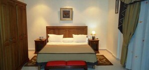 Un dormitorio con cama, mesitas de noche, un banco, un armario y un cuadro en la pared.