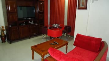 Un salon avec un canapé rouge, une table basse en bois, un téléviseur posé sur un meuble en bois et des rideaux rouges.