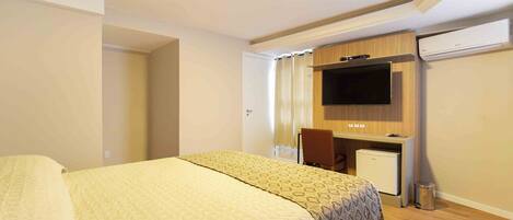 A hotel room with a bed, a desk, a chair, a television, and an air conditioning unit.