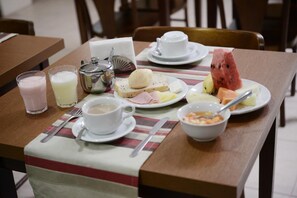 A breakfast setting with a table set for two, including plates with food, a bowl of cereal, a glass of milk, and a cup of coffee.
