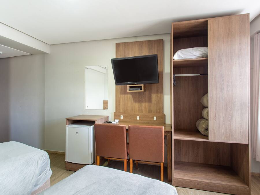 Een hotelkamer met een bed, een bureau met stoel, een televisie, een kledingkast en een kleine koelkast.