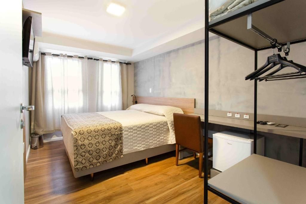 Ein Hotelzimmer mit Bett, Schreibtisch, Stuhl, Kleiderschrank und kleinem Kühlschrank.