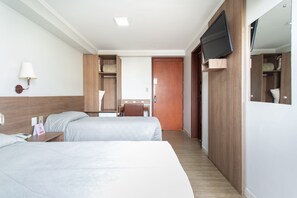 Ein Hotelzimmer mit zwei Betten, einem Schreibtisch, einem Stuhl, einem an der Wand befestigten Fernseher und einem Holzschrank.