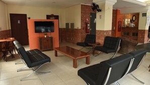 A hotel lobby with a reception desk, a flat-screen TV, a fire extinguisher, and a seating area with chairs and a table. - Hotel Dom Rafael Executivo (Santa Maria)