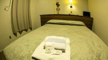 Une chambre d’hôtel avec un lit bien fait, une lampe de chevet, une table de chevet avec une horloge et une prise électrique fixée au mur.