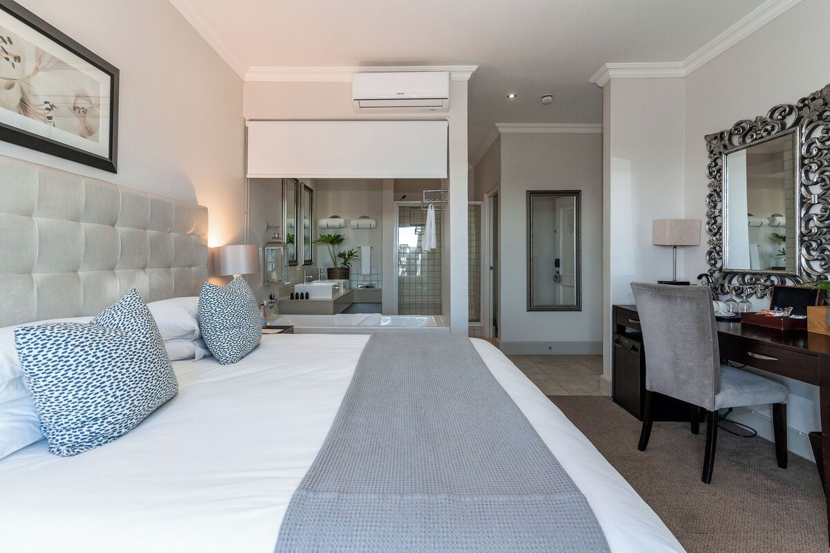 A modern hotel room with a large bed, a desk, and a bathroom visible through an open door.