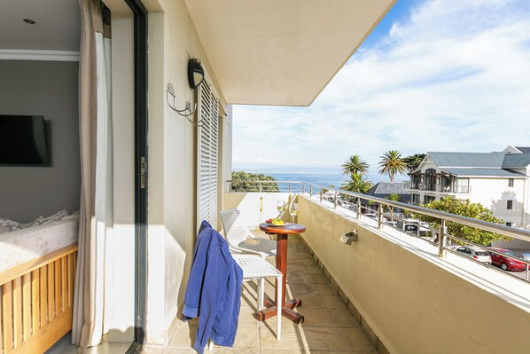 A balcony with a view of the sea, a table with a fruit bowl, and a chair.
