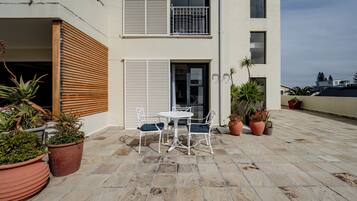 A terrace with a table and chairs, potted plants, and a building with balconies and windows.