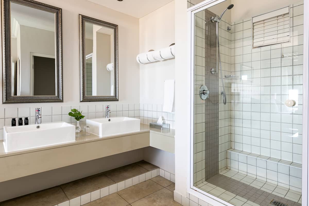 A modern bathroom with two sinks, a large mirror, and a glass-enclosed shower.