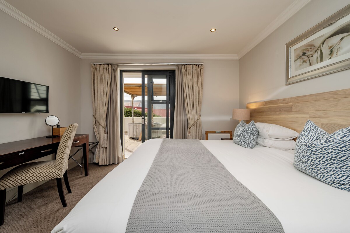 A hotel room with a large bed, a desk, a chair, a TV, and a view of the outside.