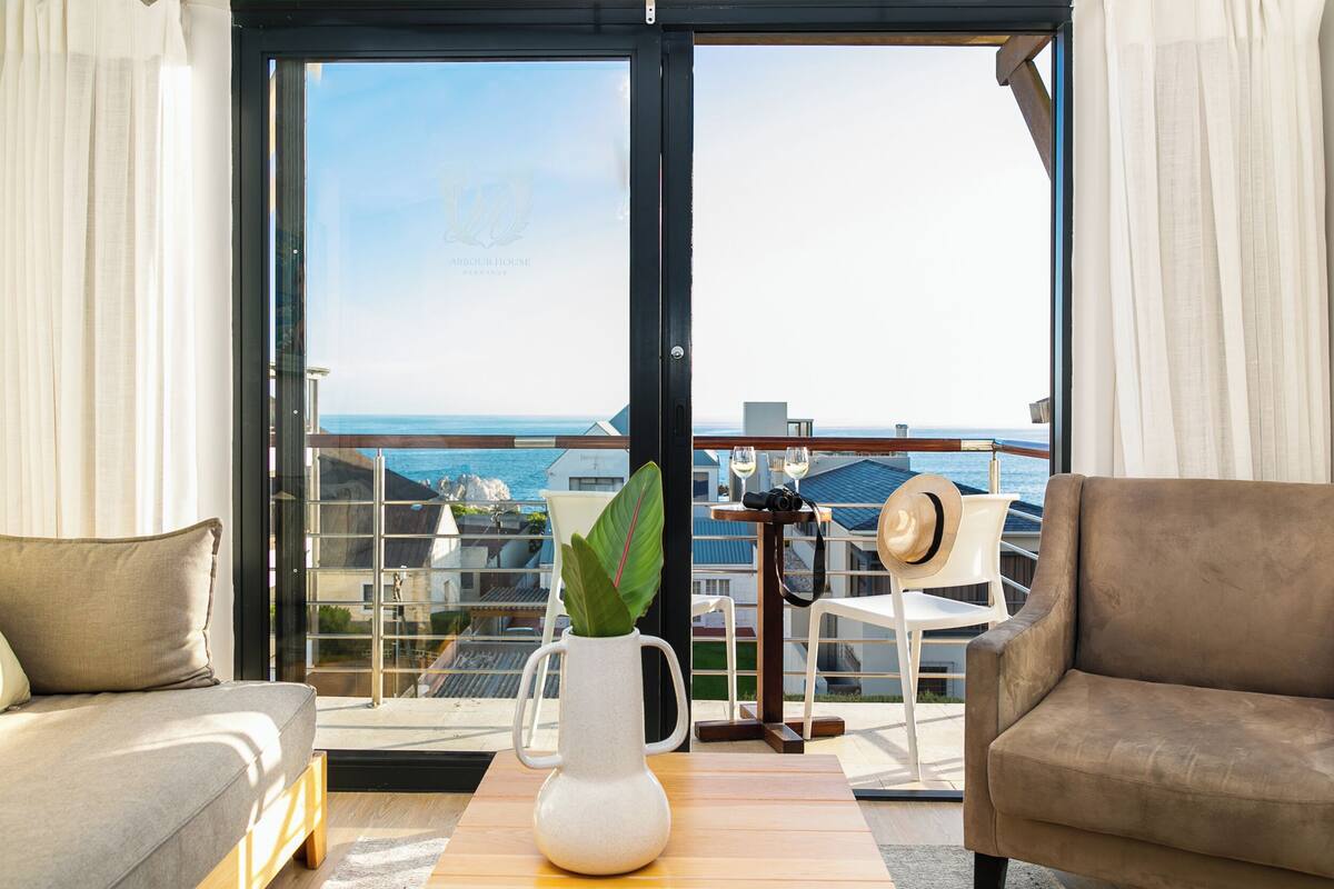 A balcony with a view of the sea, a white vase with a plant, and two sofas.