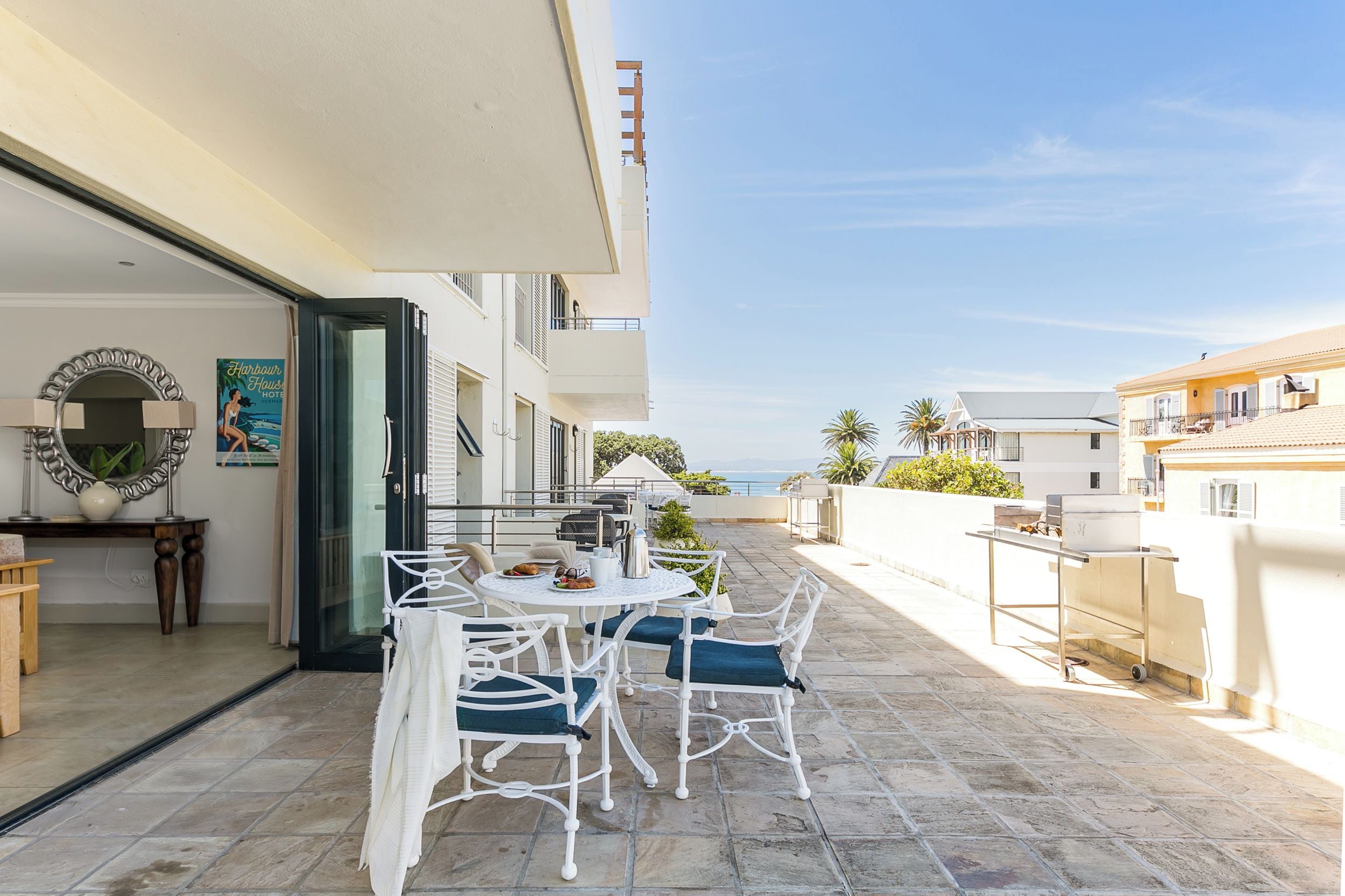 Un patio al aire libre con una mesa y sillas redondas, una parrilla y vista al mar.