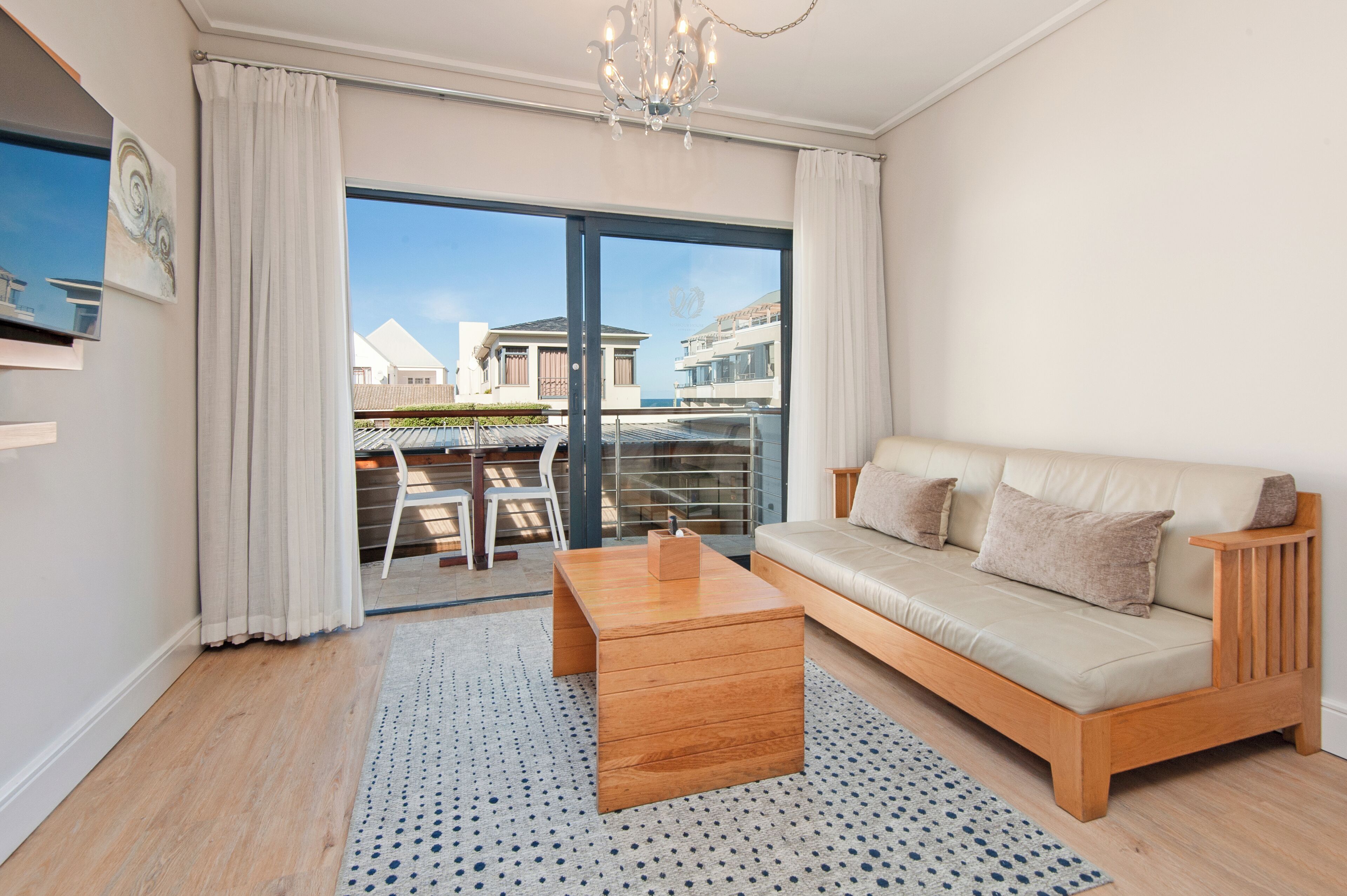 A modern living room with a sofa, coffee table, and a view of a balcony with outdoor furniture.