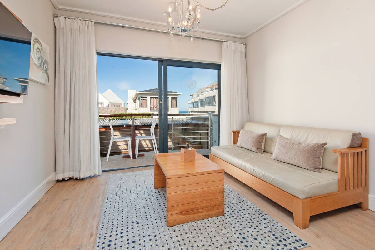 A modern living room with a sofa, coffee table, and a view of a balcony with outdoor furniture.