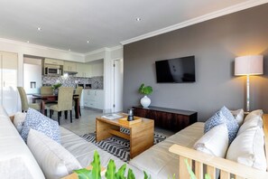 A modern living room with a sofa, coffee table, and a TV mounted on the wall. - Harbour House Hotel (Hermanus)