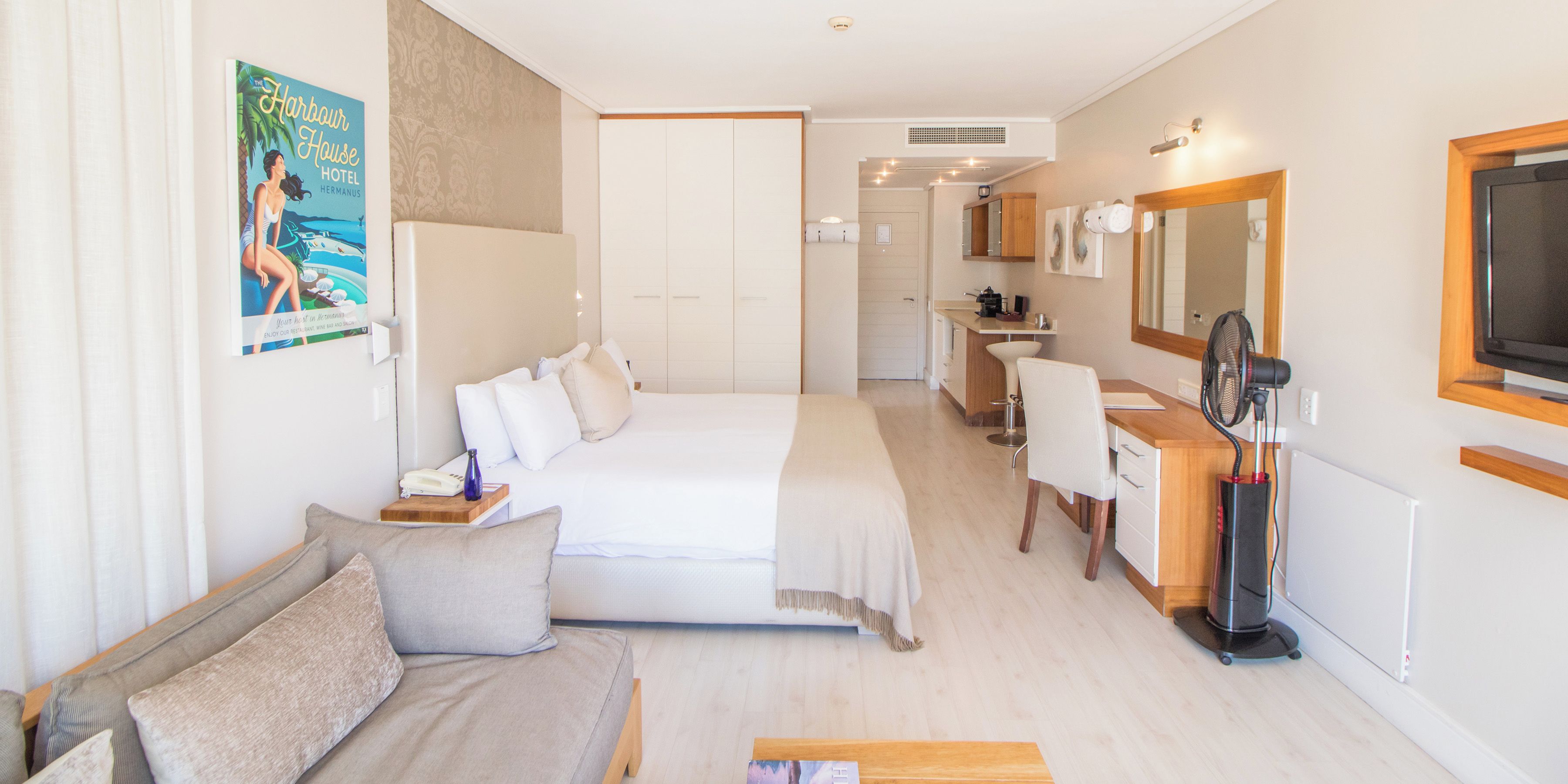 A hotel room with a bed, a sofa, a desk, a mirror, and a TV.