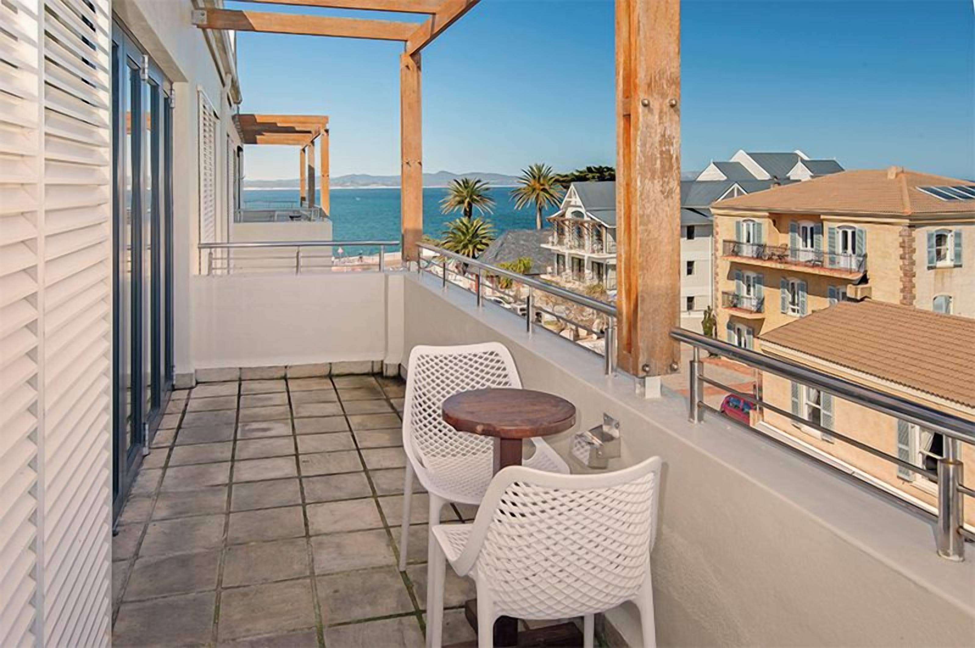 A balcony with a view of the sea, white wicker furniture, and a tiled floor.