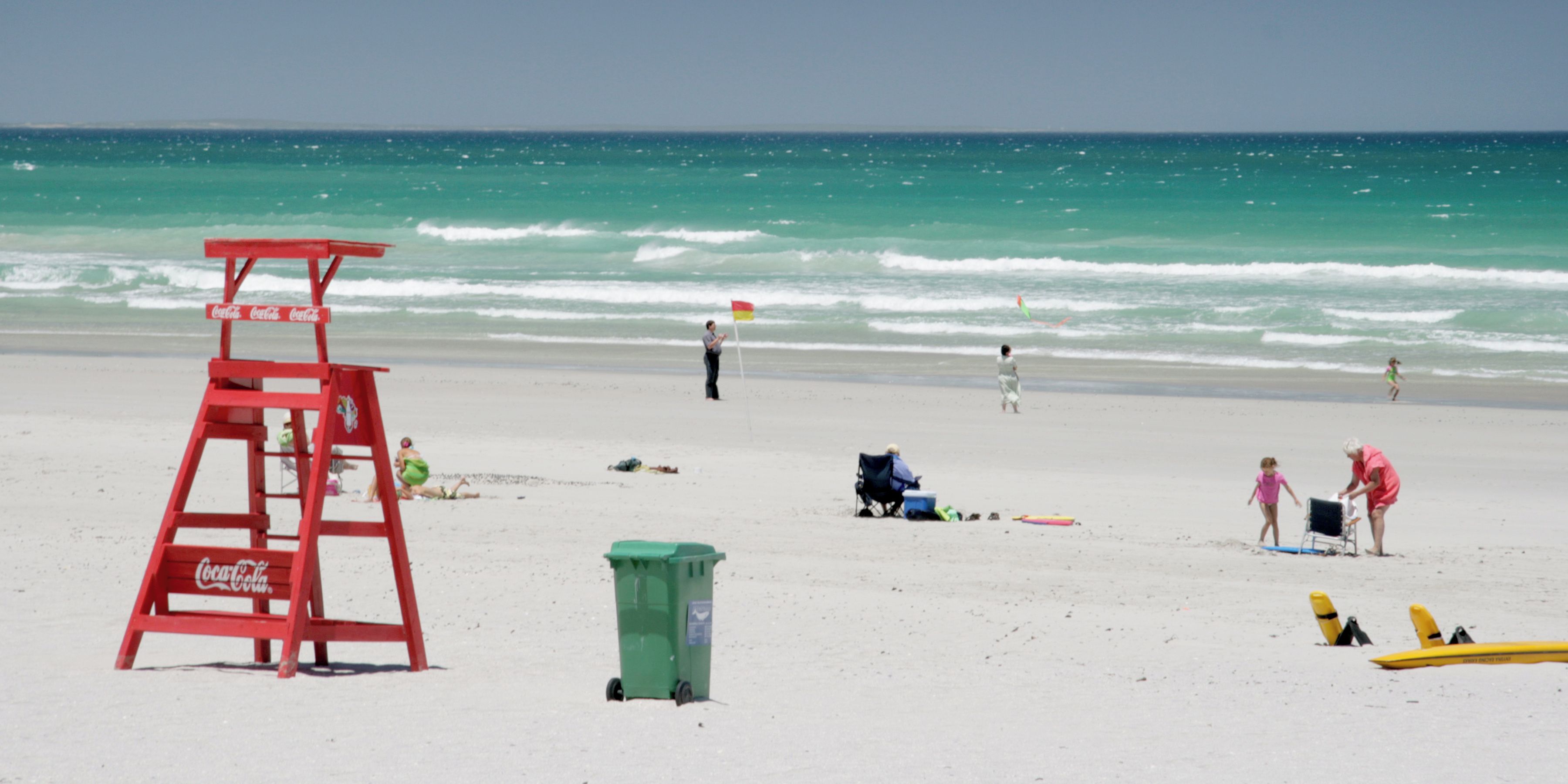 A beach with a lifeguard tower, a trash bin, and beach chairs.
