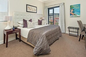 A hotel room with a large bed, a bedside table with a lamp, a chair, and a view of the outside. - Harbour House Hotel (Hermanus)