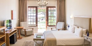 A hotel room with a bed, two chairs, a desk, a television, and a view of the outdoors through large windows. - Harbour House Hotel (Hermanus)